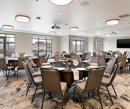 A banquet room filled with round tables and chairs. The tables are set with pitchers of water in the middle.