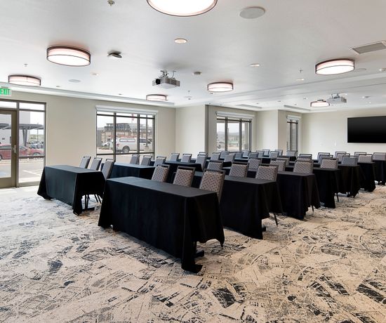 Long tables with black tablecloths and chairs on one side, all facing one end of the large event room.
