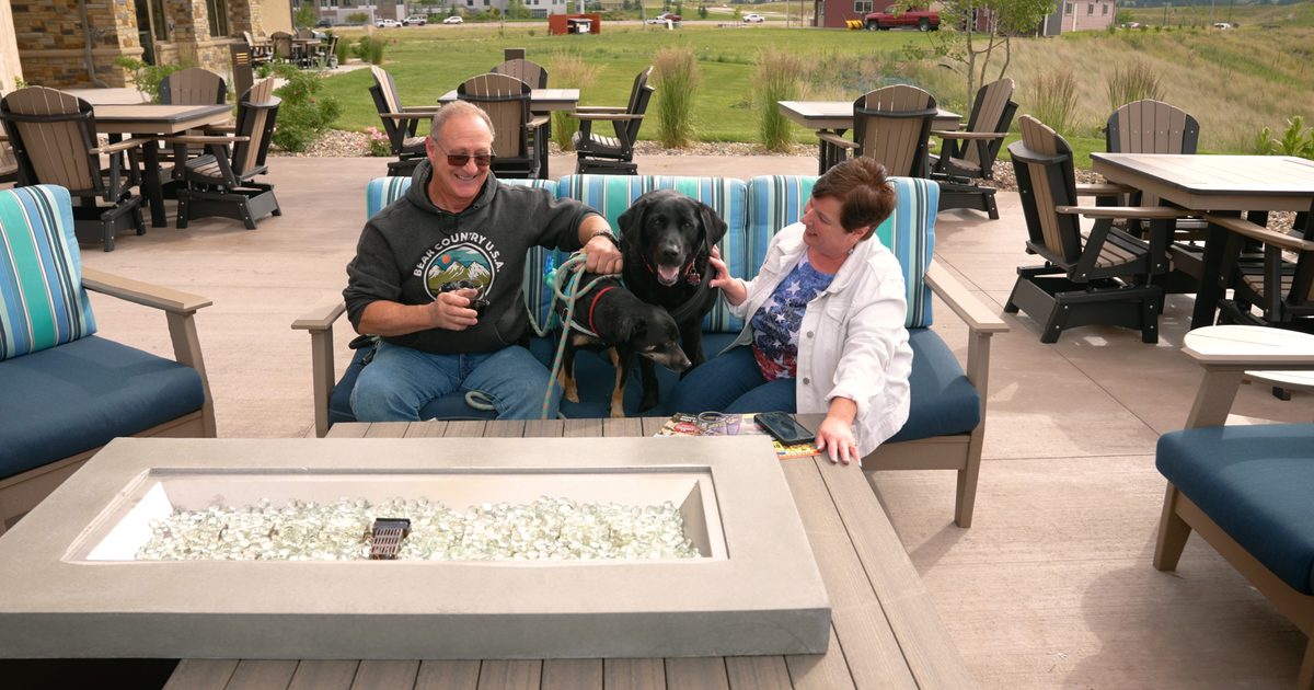 A couple outside with their two dogs by the fire pit with a glass of wine