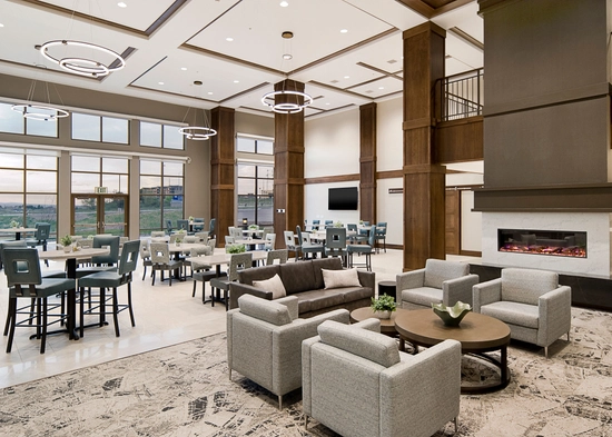 A large room with tables and chairs near windows, and chairs and couches near the fireplace on the other end of the space.