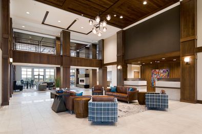 The lobby wiht chairs and couches set up in the middle and the front desk to the right. There is ane xposed walkway on the second floor that looks down on the lobby.