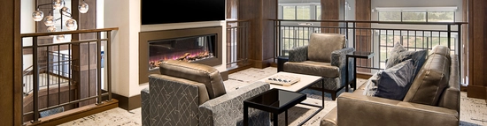 A couch and two chairs sitting in front of a fireplace with railings around it, as it's a landing on the second floor.